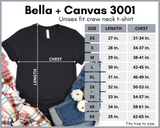 Bella Canvas unisex sit crew neck tshirt size chart with black shirt on the left with chest and length measurements surrounded by a flannel shirt in orange and beige, jeans to the right and small pumpkins in white.  Chart has size, lengh and chest.