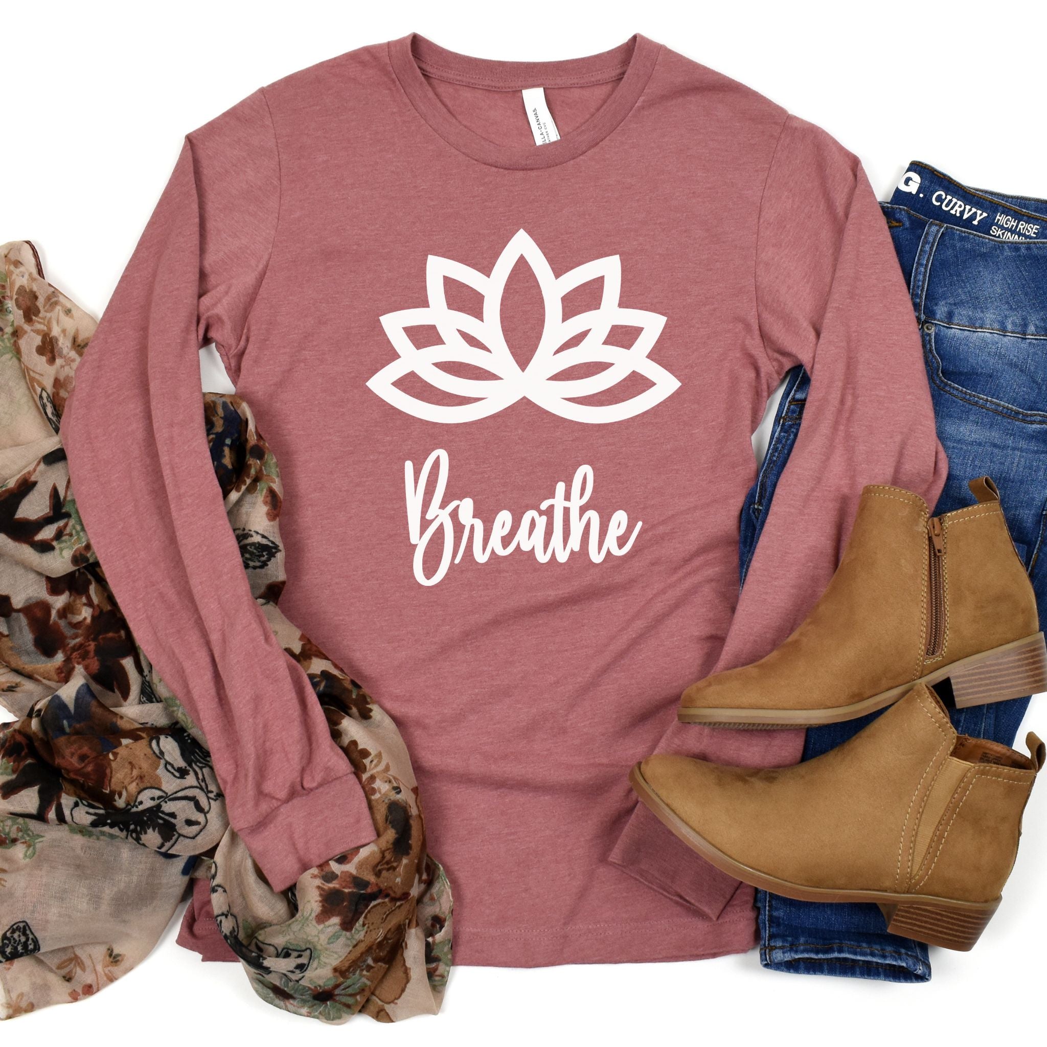 Heather Mauve Long Sleeve shirt in center with white Lotus flower and word Breathe underneath on shirt.  Shirt surrounded by a scarf to the left and blue jeans with brown ankle boots to the right.