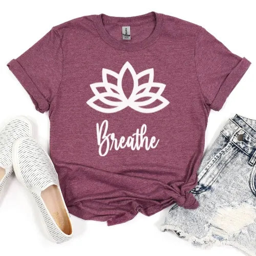 Maroon t-shirt with white lotus flower and 'Breathe' text, paired with white sneakers and denim shorts on a light gray background.