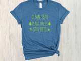 A heather blue short-sleeve t-shirt with rolled cuffs and a knotted hem, featuring a lime green graphic print that reads 'CLEAN SEAS PLANT TREES SAVE BEES' with small tree and bee illustrations. The shirt is laid flat on a light wood background.