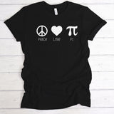 A black short-sleeve t-shirt laid flat on a white wood plank background, featuring a white graphic print of a peace symbol, a heart, and a pi symbol with the words 'PEACE', 'LOVE', and 'PI' underneath.