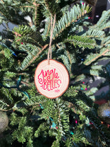 A round wooden Christmas ornament hanging on a green evergreen tree. The ornament is light natural wood with red lettering that reads 'Jingle Bells 2024' and is suspended by a thin string.