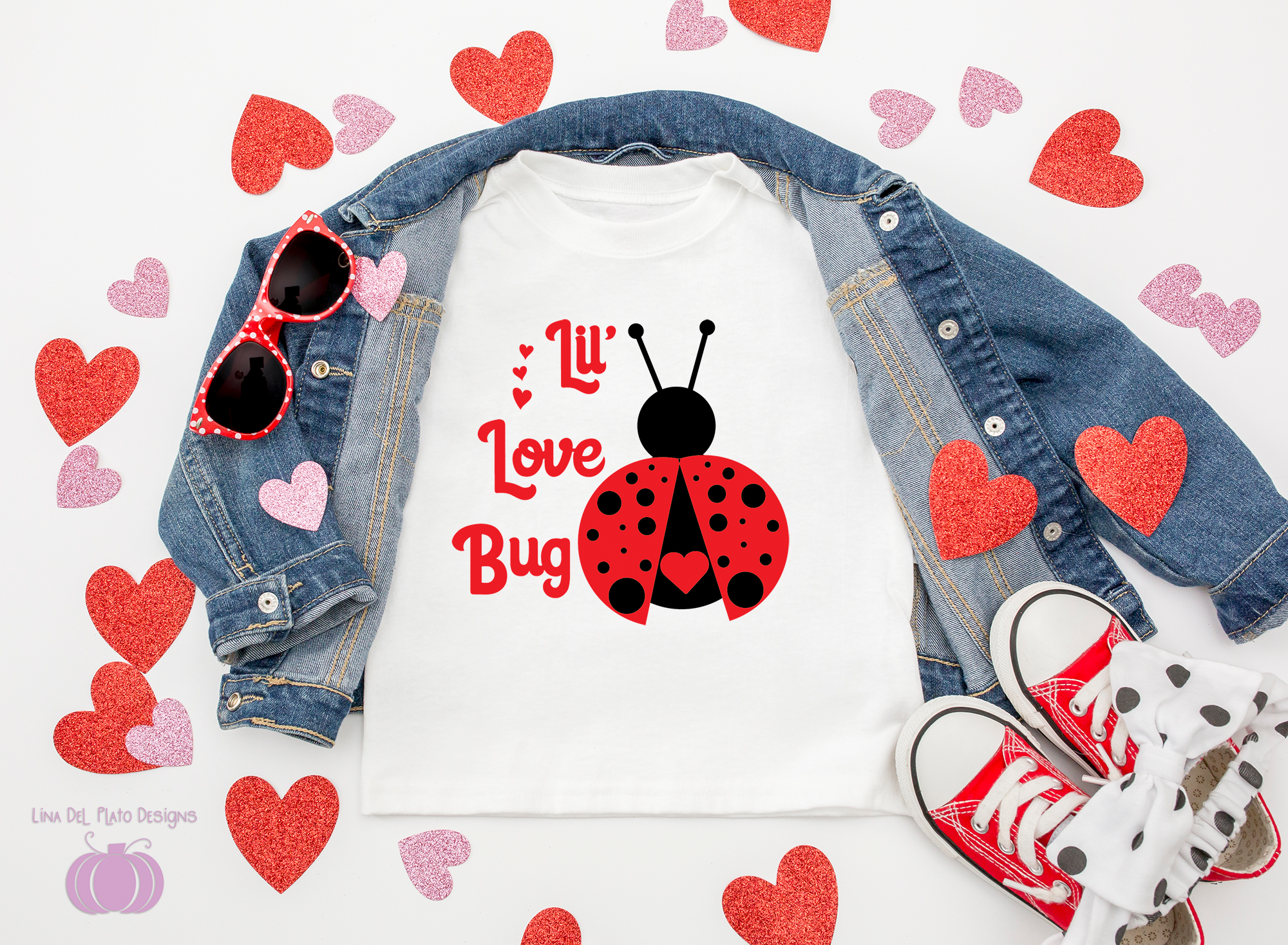A flat-lay of a white graphic T-shirt with a red ladybug and the words 'I'll Love Bug' in red, styled with an open blue denim jacket, red sunglasses, red and white sneakers, and scattered red and pink glitter hearts on a white background.
