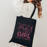 A woman wearing a white sweatshirt carries a black canvas tote bag with pink text that reads 'Of course I do Math like a GIRL do try to keep up' against a plain light background.