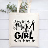 An off-white canvas tote bag with black printed text that reads 'Of course I do Math like a GIRL do try & keep up' and a chalkboard graphic, hanging against a white wood plank background with green leaves at the top.