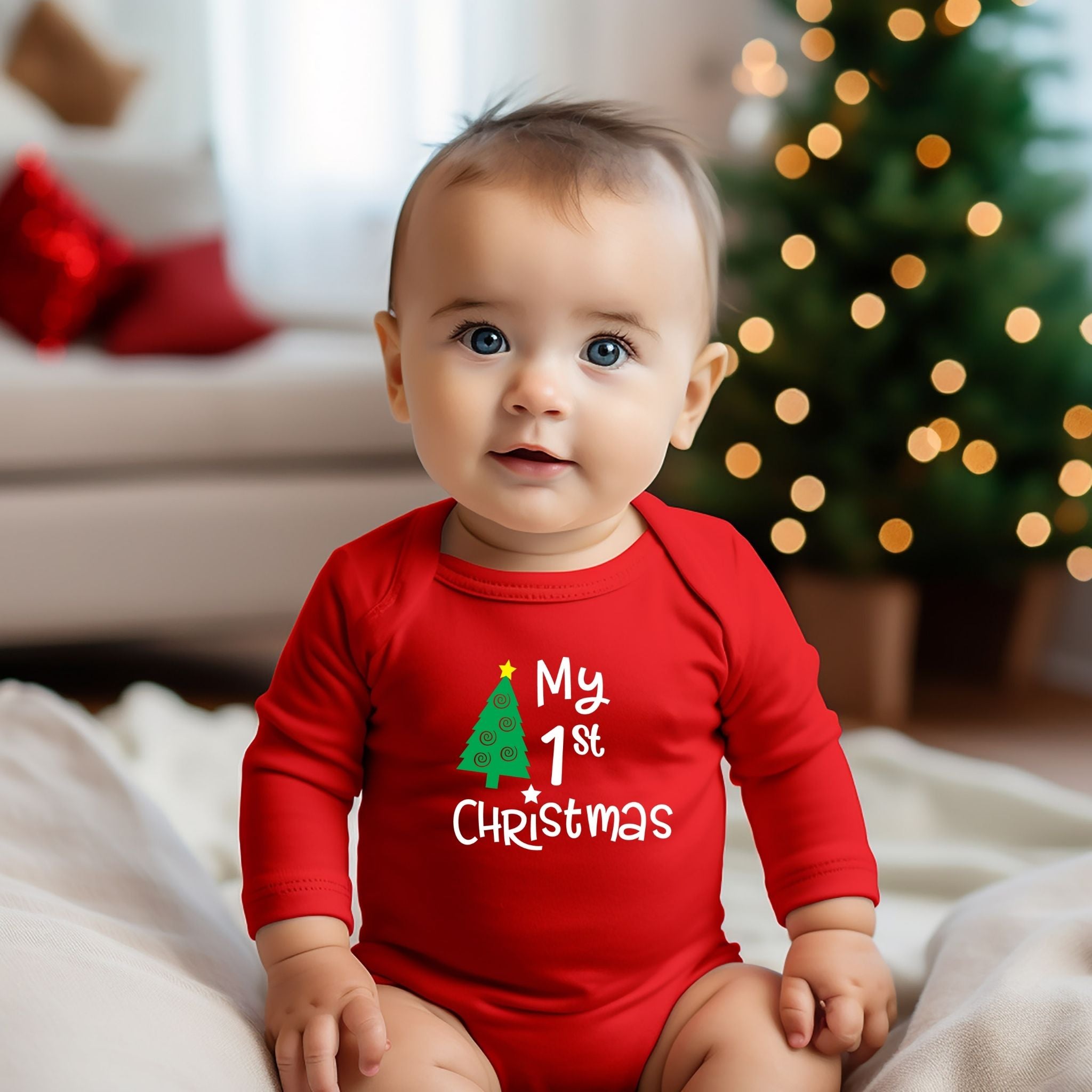 A baby wearing a red long-sleeve bodysuit with a 'My 1st Christmas' graphic, sitting in a cozy living room with a blurred Christmas tree in the background.