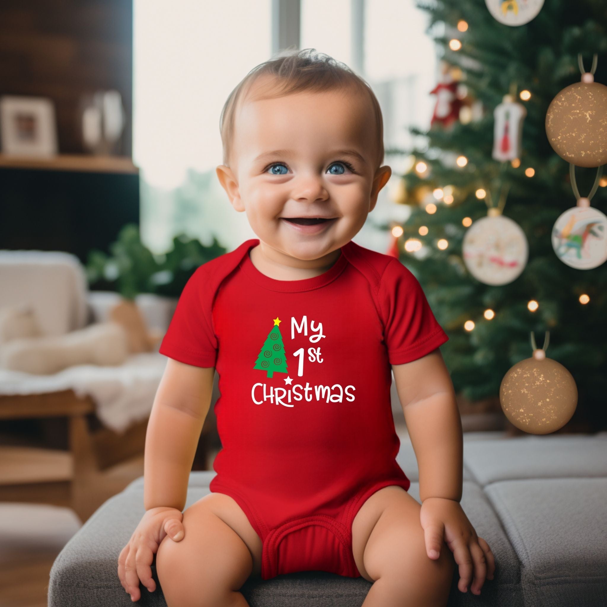 A baby wearing a red short-sleeve bodysuit with 'My 1st Christmas' and a green tree graphic, sitting on a gray sofa in front of a decorated Christmas tree.