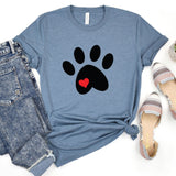 A heathered blue short-sleeve T-shirt laid flat with a black paw print graphic and a small red heart in the center. The shirt is styled in a flat lay with blue jeans on the left and patterned slip-on shoes on the right against a white background.