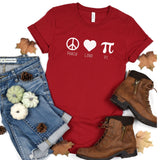 Red shirt with white Peace Love Pi wititen.  Jeans to the left with pumpkins in white and green, fall leaves, and brown boots to the right.