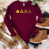 A long-sleeve maroon shirt laid flat on a rustic wood surface, featuring a yellow triangle pattern across the chest. The shirt is styled with a plaid flannel shirt, dark jeans, brown lace-up boots, and green leaves.