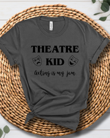 A dark gray graphic t-shirt with black text reading 'THEATRE KID acting is my jam' and theatrical mask icons, styled on a round woven straw mat.