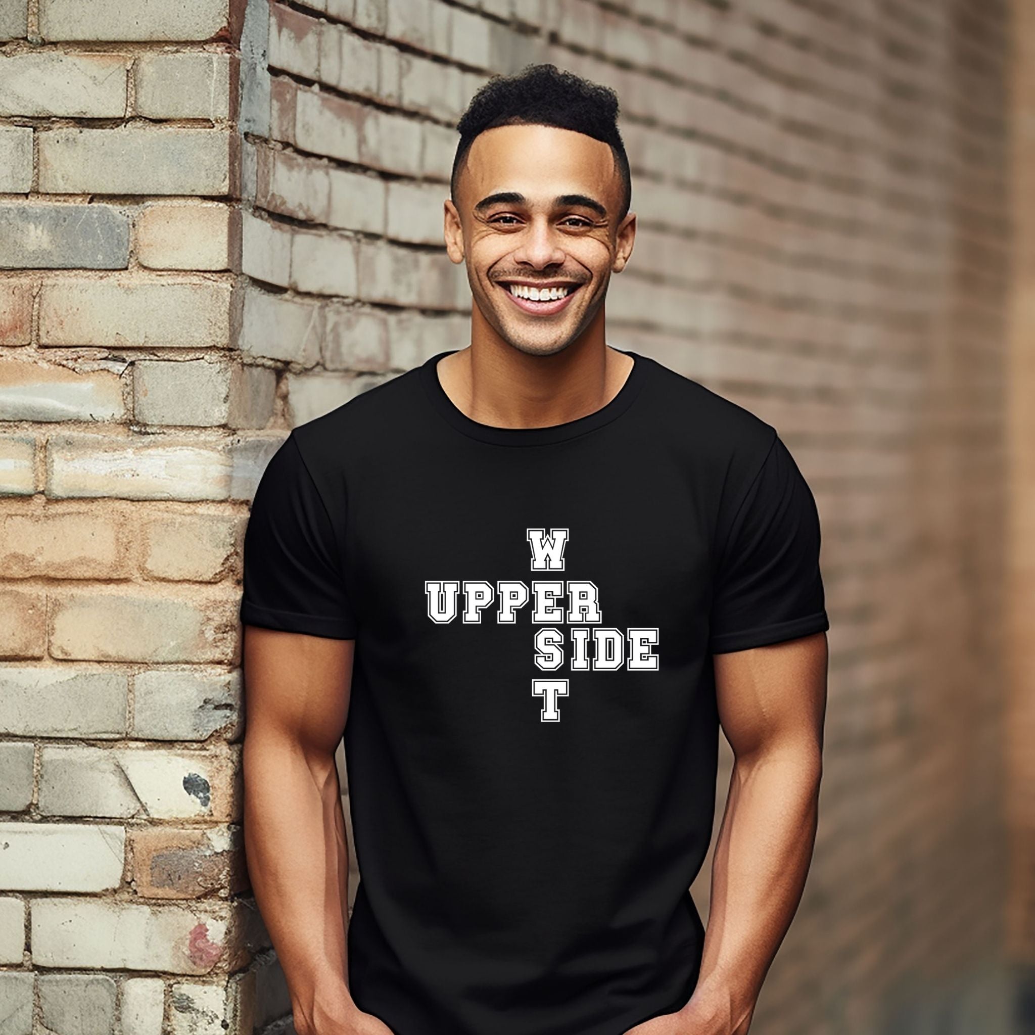 A smiling man wearing a black t-shirt with a white graphic text design that reads 'W UPPER SIDE T' in a cross layout, standing against a brick wall.